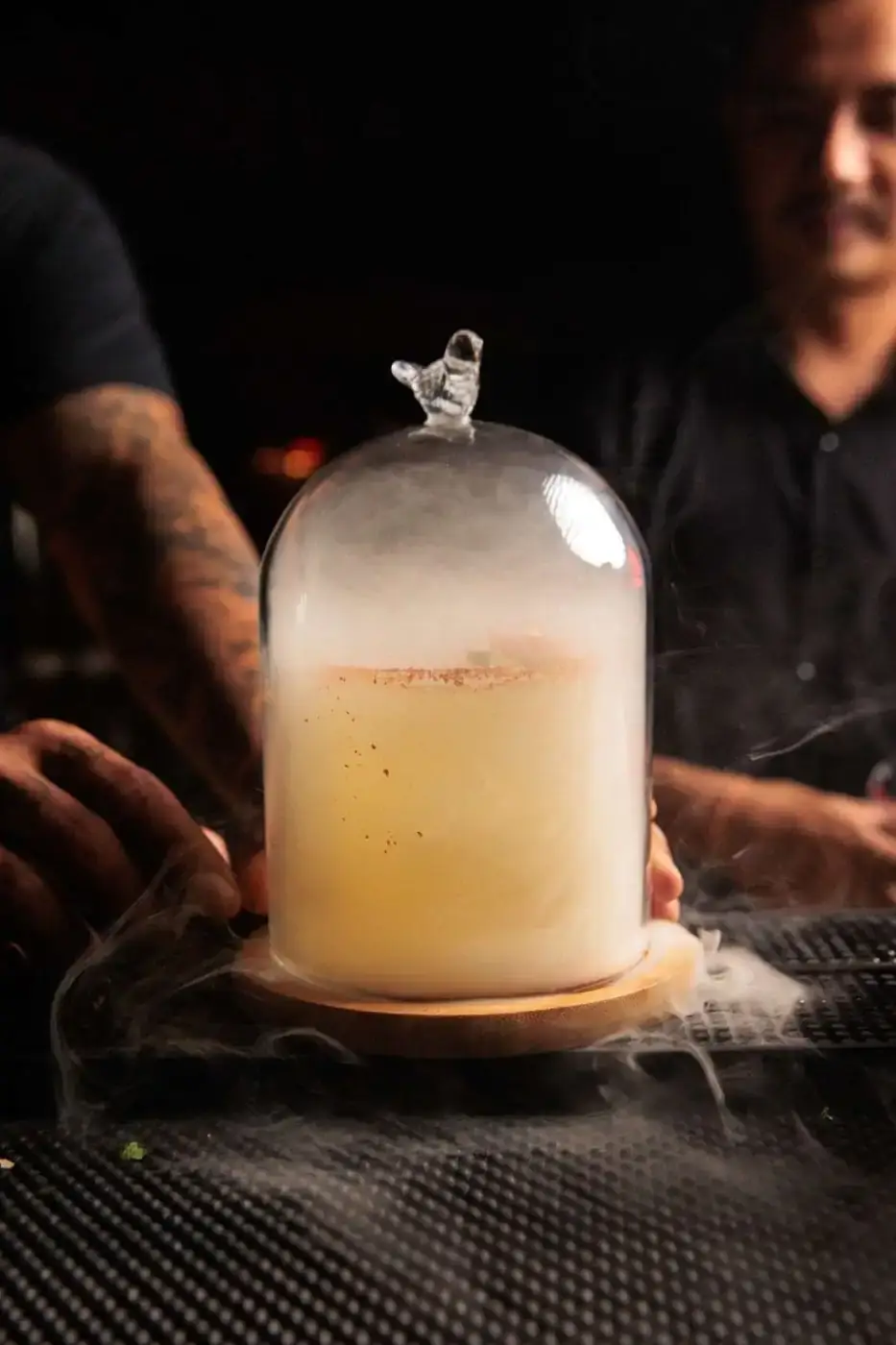A cocktail served under a smoke-filled glass cloche
