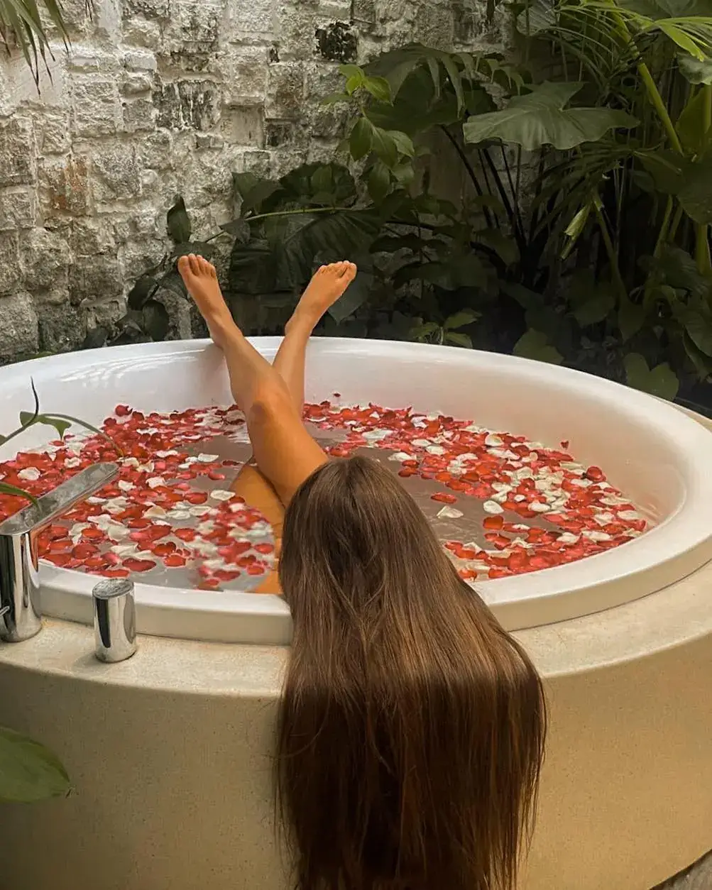 Flower-strewn round bathtub, a guest's legs raised over the rim