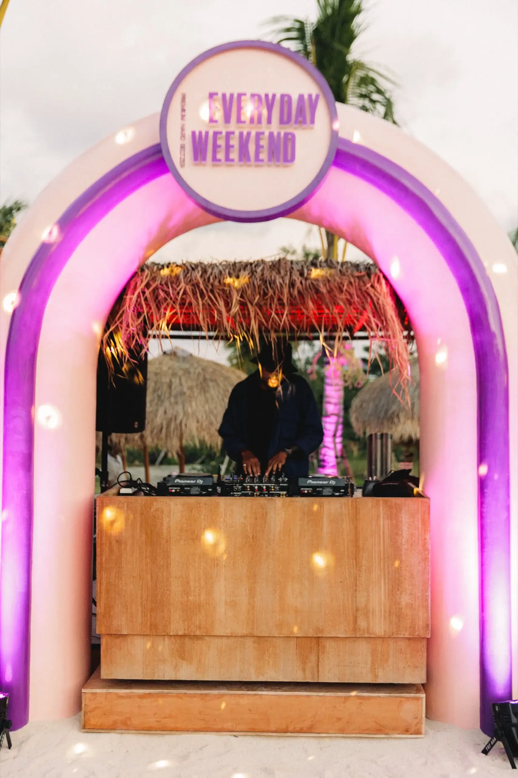 The DJ booth built inside a pink-lit arch with an illuminated EVERYDAY WEEKEND sign mounted above it