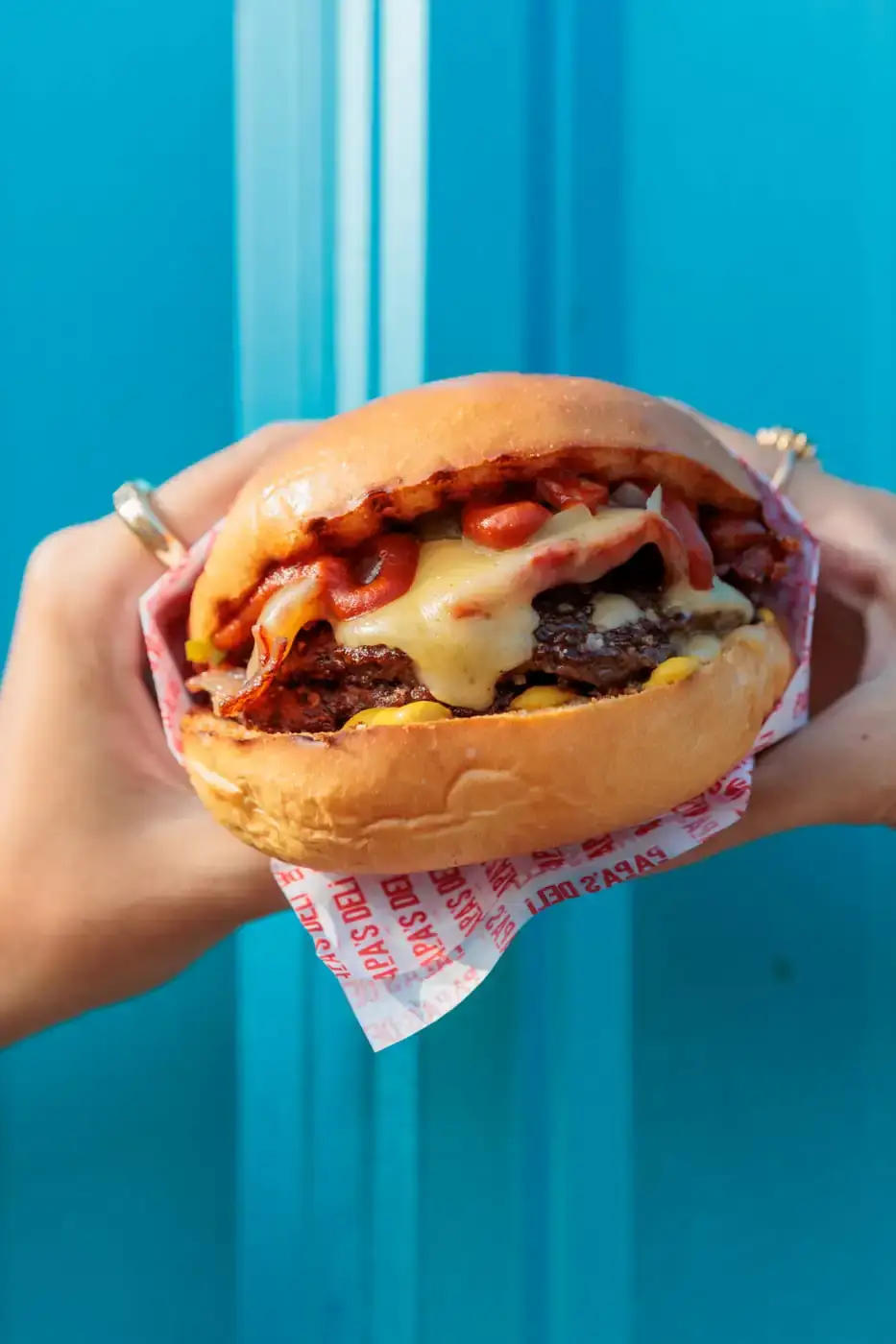 Burger held in its wrapper against a bright cyan wall
