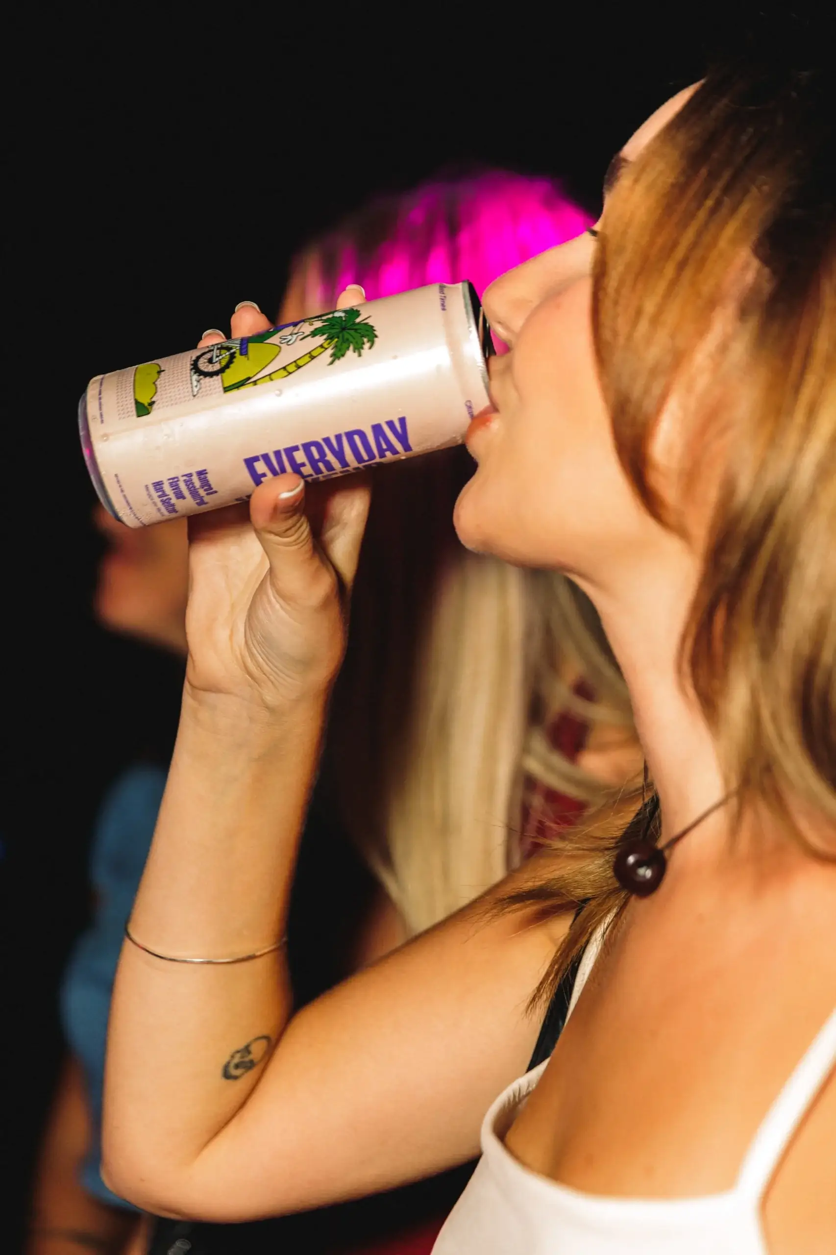 A guest drinking straight from a Lime & Soda can, the wordmark facing the camera under magenta light