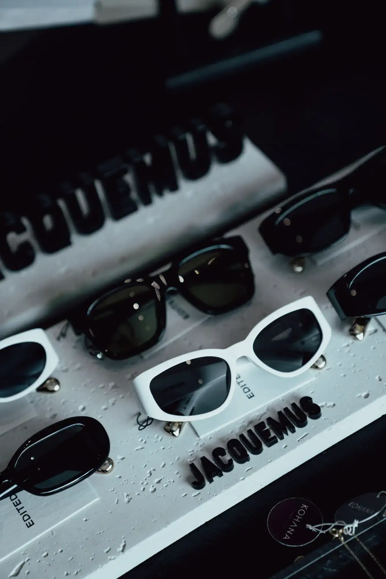 Sunglasses lined up on a concrete shelf under a Jacquemus header