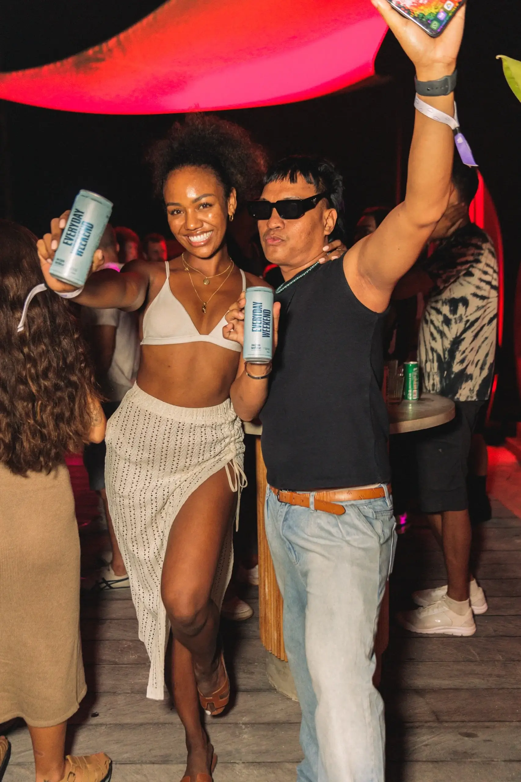 Two guests dancing with cans raised under the red and pink canopy