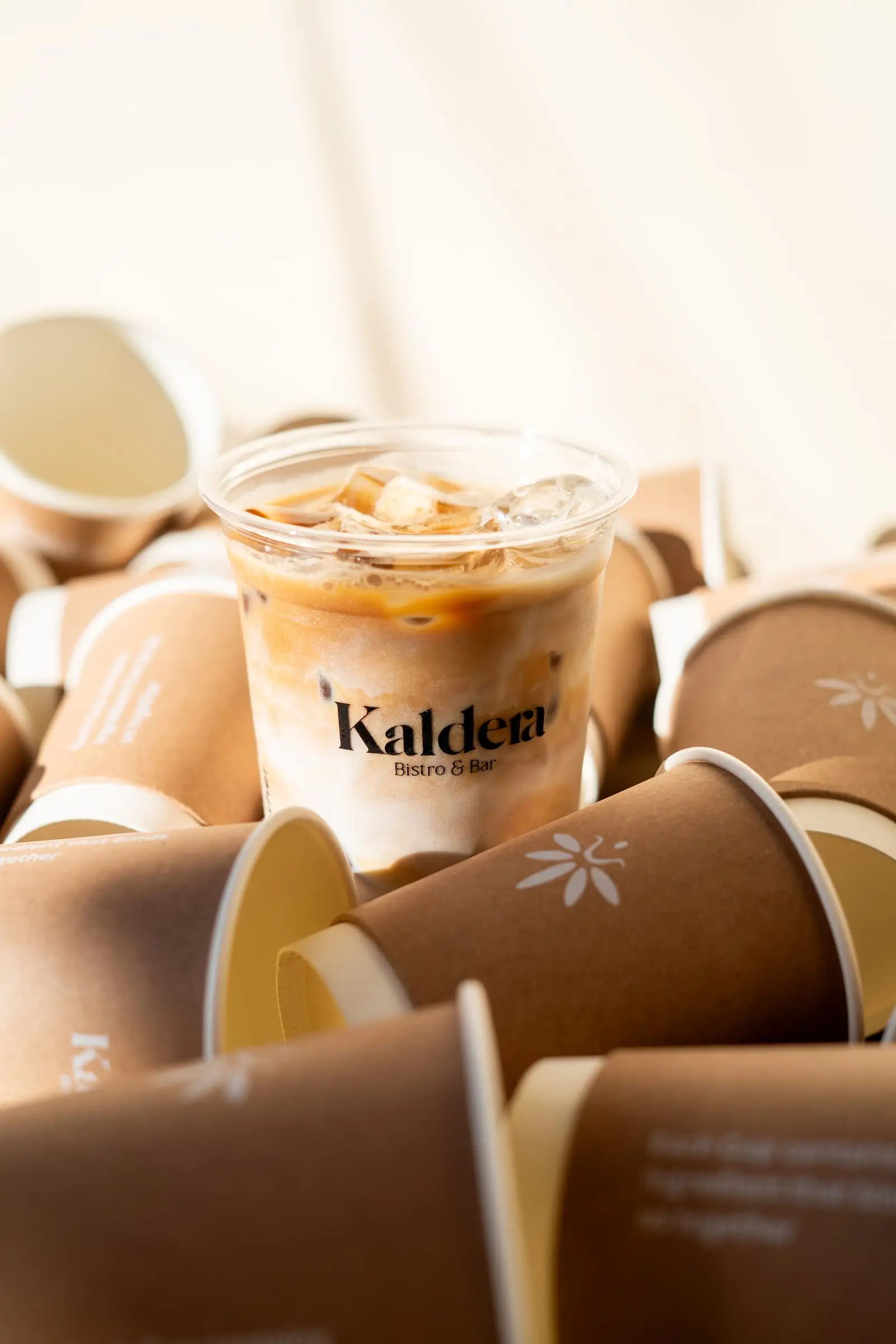 Branded iced coffee cup among paper cups in warm sunlight