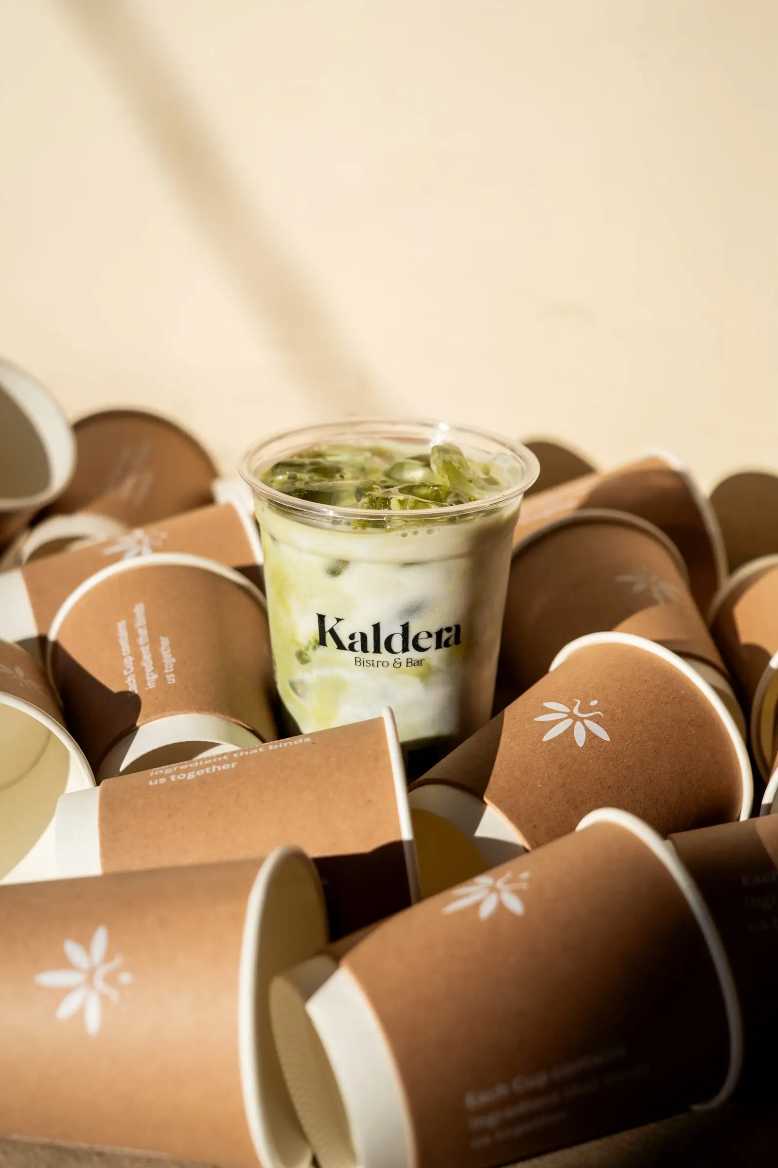 Minuman matcha dingin dalam gelas bermerek di antara gelas kertas