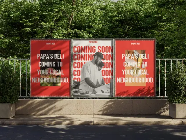 Tiga poster pra-peluncuran Papa's Deli ditempel berdampingan di pagar proyek pinggir jalan — dua lembar merah 'coming to your local neighbourhood' mengapit poster hitam-putih COMING SOON — Papa's Deli
