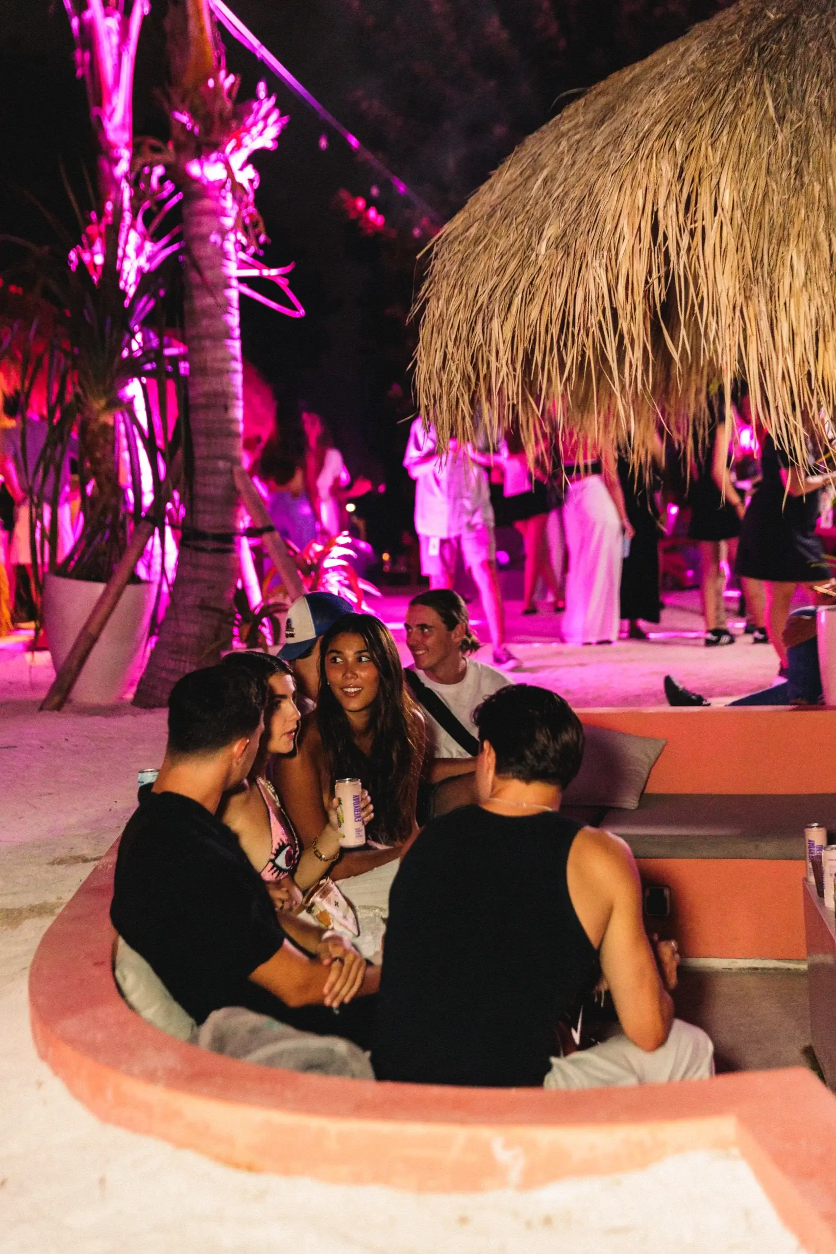 Guests sitting around the sunken terracotta lounge, the whole terrace washed magenta