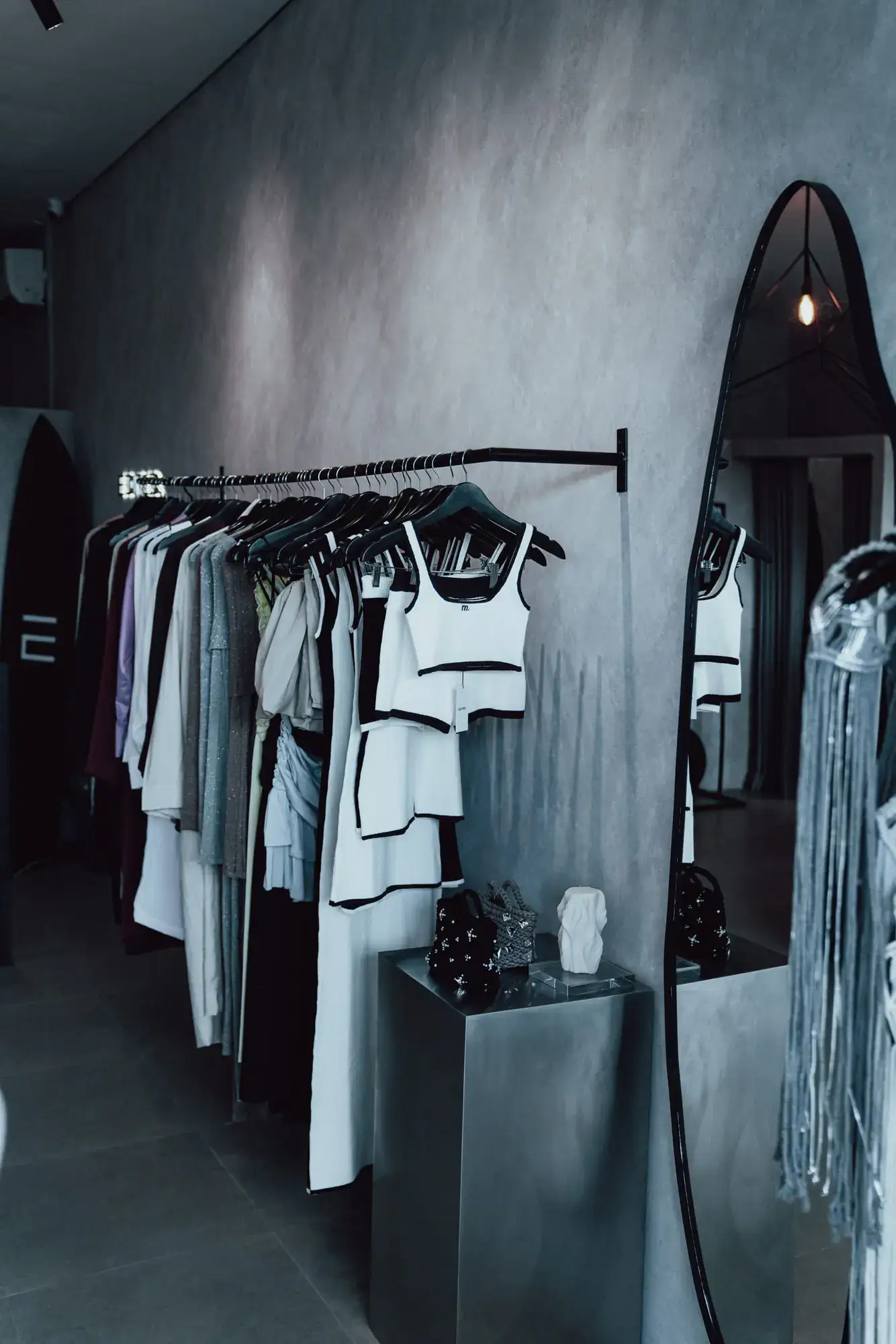 A rail of pale garments along a concrete wall, arched mirror at the end