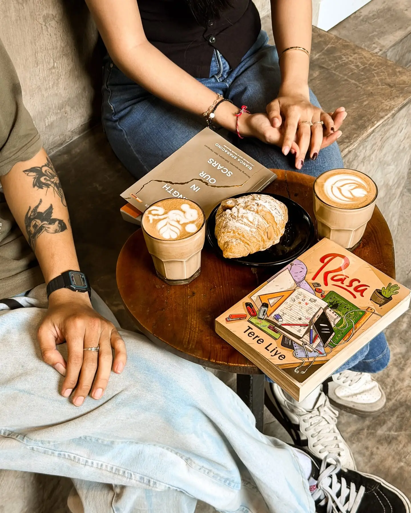 Kopi, croissant, dan buku di meja kayu bundar, gaya lifestyle